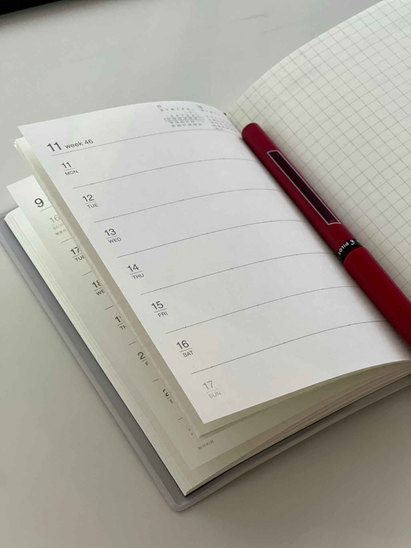 Open weekly planner showing dates and weekdays, with a red pen resting across lined pages.