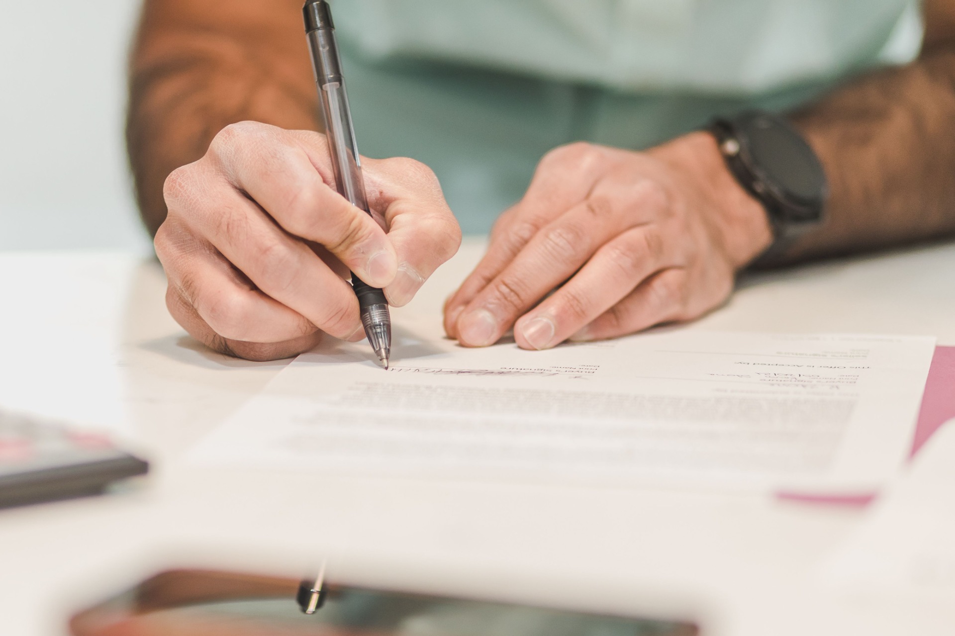 Hands signing a document with a pen on a desk, close-up with blurred background.