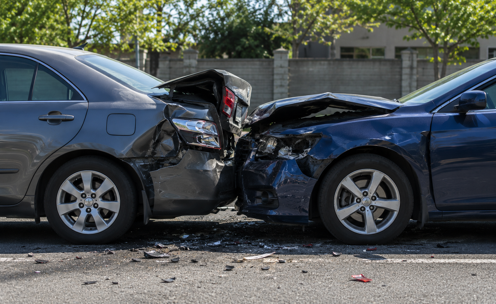 Two damaged cars with crumpled front ends, broken headlights, and debris on asphalt outdoors.