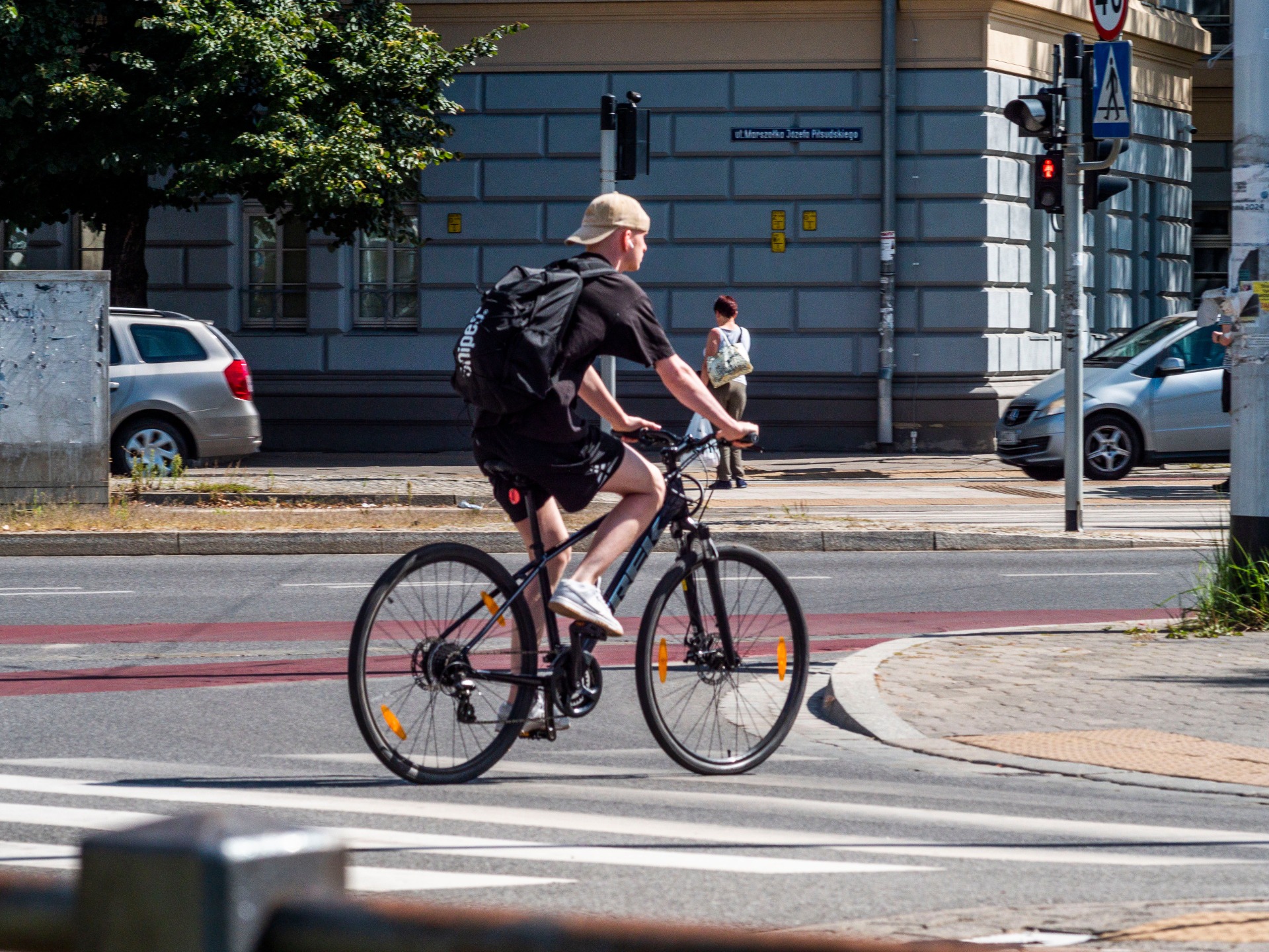 Cyclist in black rides a bicycle past cars and a traffic light on a city street.