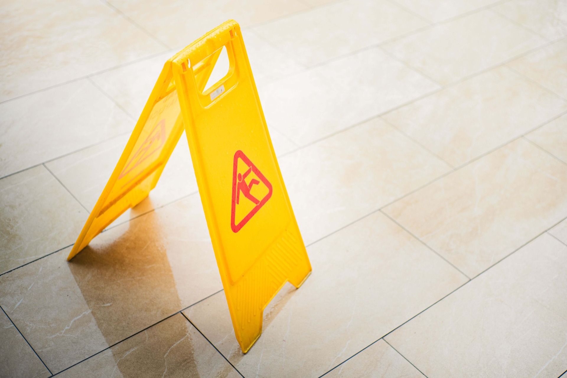 Yellow caution sign with red warning symbol standing on tiled floor, angled toward camera.