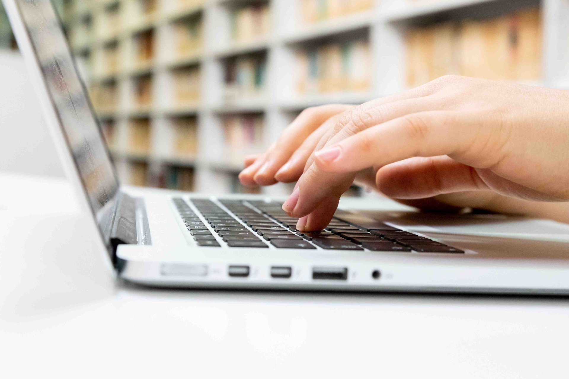 Hand typing on a laptop keyboard, close-up with blurred office background.