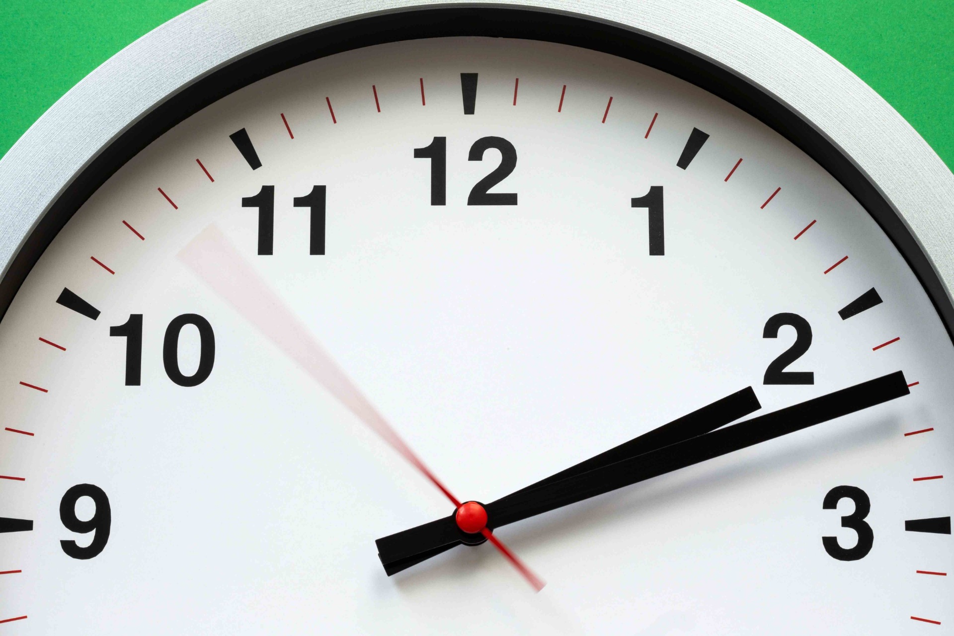 Close-up of a clock face showing 12 with black hands, red ticks, and green background.