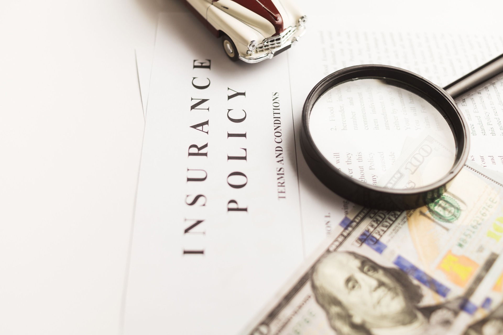 Magnifying glass over documents labeled “Insurance” and “Policy,” with a vintage car model in background.