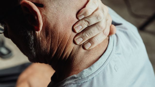 Man holds his neck with one hand, showing pain and discomfort. Close up on hand holding neck.