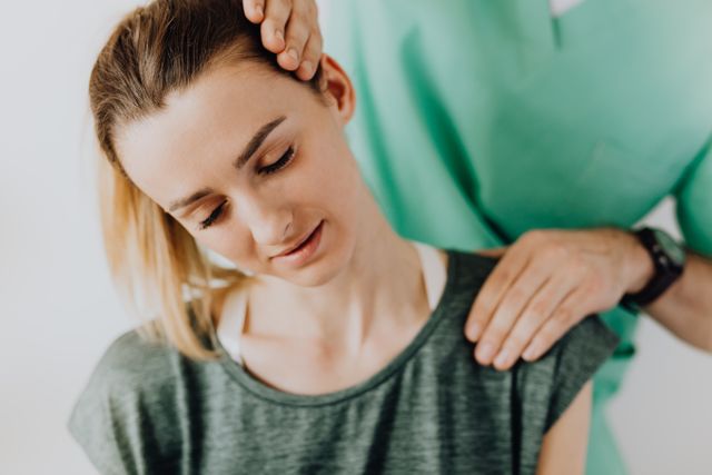 Woman gently holding her neck, eyes closed, wearing a green shirt and smartwatch, suggesting discomfort.