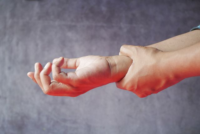 Two hands showing someone in pain with an outstretched forearm against a blurred gray background.