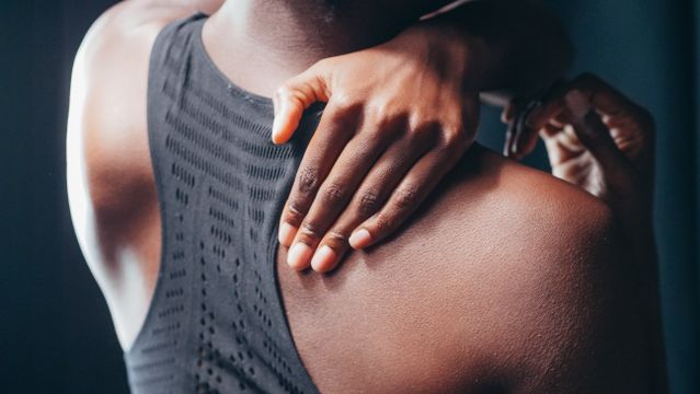 Hand gently presses a person’s shoulder, suggesting pain or massage, with soft lighting and close framing.